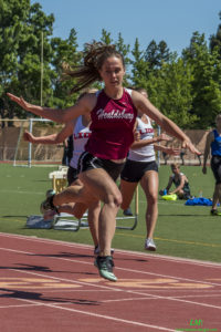 Athlete prepares for pole vault on a track with others watching.