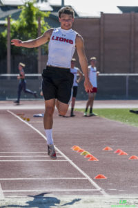 Athlete prepares for pole vault on a track with others watching.