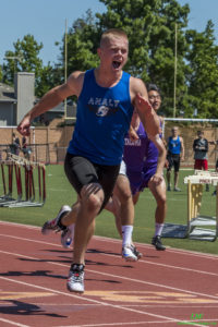 Athlete prepares for pole vault on a track with others watching.