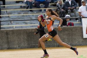 Athlete prepares for pole vault on a track with others watching.