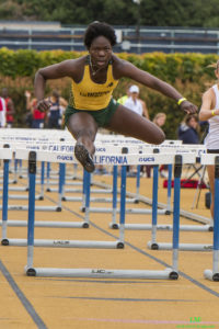 Athlete prepares for pole vault on a track with others watching.