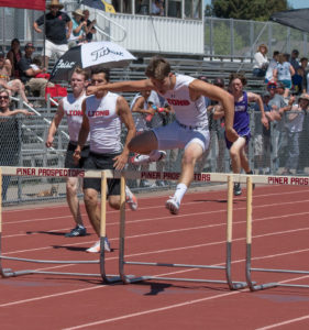 Athlete prepares for pole vault on a track with others watching.