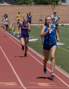 Athlete prepares for pole vault on a track with others watching.