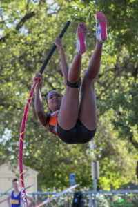 Athlete prepares for pole vault on a track with others watching.