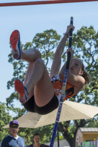 Athlete prepares for pole vault on a track with others watching.