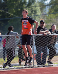 Athlete prepares for pole vault on a track with others watching.