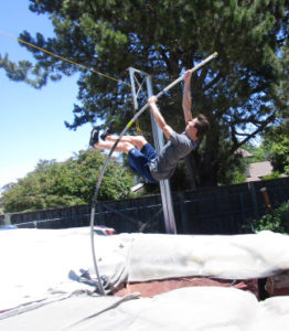 Athlete prepares for pole vault on a track with others watching.