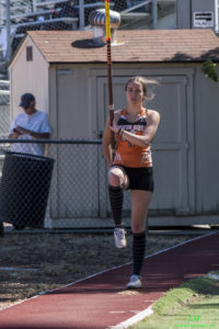 Athlete prepares for pole vault on a track with others watching.