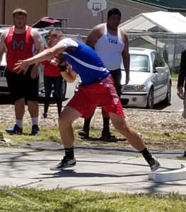 Athlete prepares for pole vault on a track with others watching.