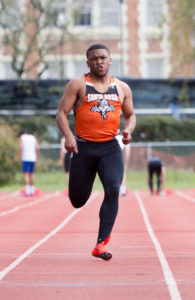 Athlete prepares for pole vault on a track with others watching.