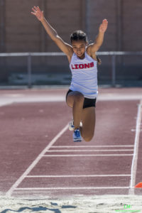 Athlete prepares for pole vault on a track with others watching.
