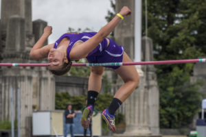 Athlete prepares for pole vault on a track with others watching.