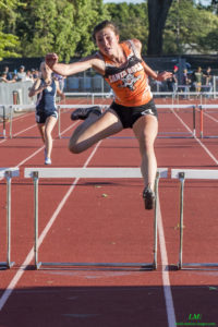Athlete prepares for pole vault on a track with others watching.