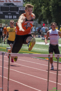 Athlete prepares for pole vault on a track with others watching.