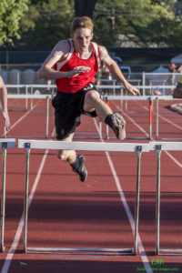 Athlete prepares for pole vault on a track with others watching.