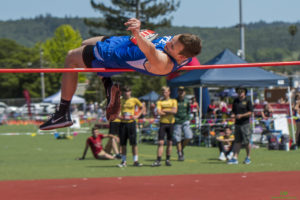 Athlete prepares for pole vault on a track with others watching.
