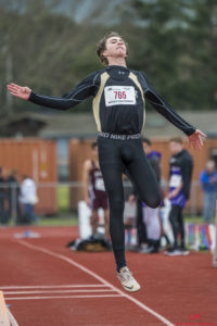 Athlete prepares for pole vault on a track with others watching.