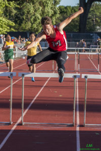 Athlete prepares for pole vault on a track with others watching.