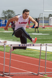 Athlete prepares for pole vault on a track with others watching.