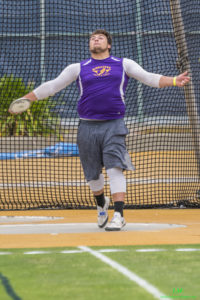 Athlete prepares for pole vault on a track with others watching.