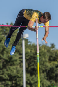 Athlete prepares for pole vault on a track with others watching.