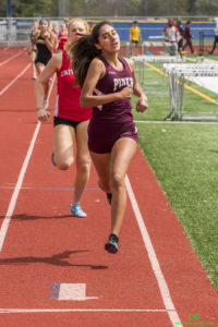 Athlete prepares for pole vault on a track with others watching.