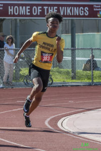 Athlete prepares for pole vault on a track with others watching.