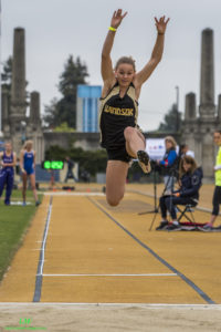 Athlete prepares for pole vault on a track with others watching.