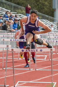 Athlete prepares for pole vault on a track with others watching.