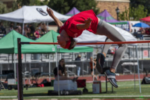 Athlete prepares for pole vault on a track with others watching.