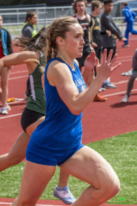 Athlete prepares for pole vault on a track with others watching.