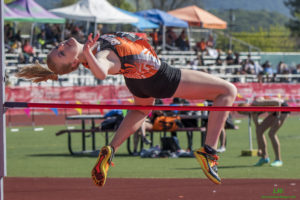 Athlete prepares for pole vault on a track with others watching.