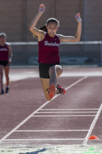 Athlete prepares for pole vault on a track with others watching.