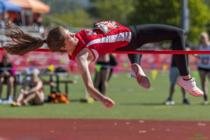Athlete prepares for pole vault on a track with others watching.