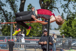 Athlete prepares for pole vault on a track with others watching.