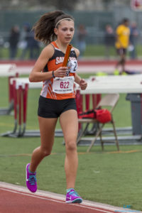 Athlete prepares for pole vault on a track with others watching.