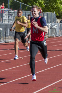 Athlete prepares for pole vault on a track with others watching.