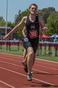 Athlete prepares for pole vault on a track with others watching.