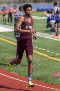 Athlete prepares for pole vault on a track with others watching.