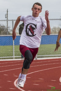 Athlete prepares for pole vault on a track with others watching.