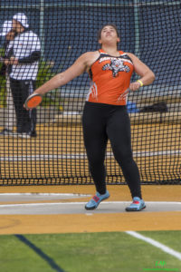 Athlete prepares for pole vault on a track with others watching.