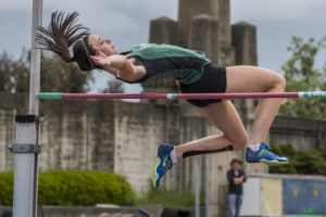 Athlete prepares for pole vault on a track with others watching.