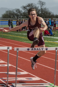 Athlete prepares for pole vault on a track with others watching.
