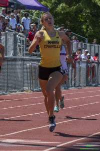 Athlete prepares for pole vault on a track with others watching.