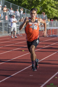 Athlete prepares for pole vault on a track with others watching.