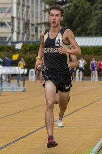 Athlete prepares for pole vault on a track with others watching.