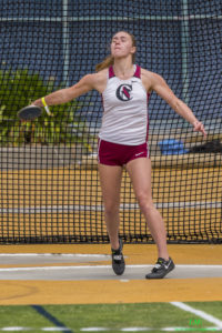 Athlete prepares for pole vault on a track with others watching.