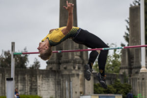 Athlete prepares for pole vault on a track with others watching.