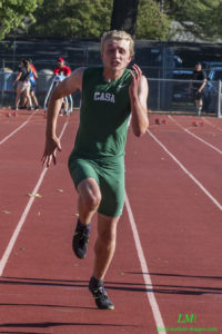 Athlete prepares for pole vault on a track with others watching.