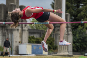 Athlete prepares for pole vault on a track with others watching.